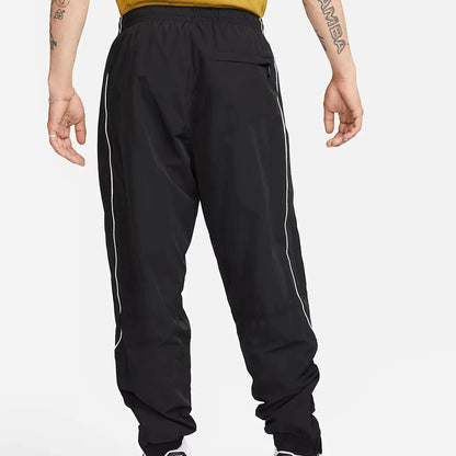 Nike Solo Swoosh Men’s Track Pants in black, back view. Shows secure zip pocket, reflective piping along legs, adjustable cuffs and lightweight nylon fabric.